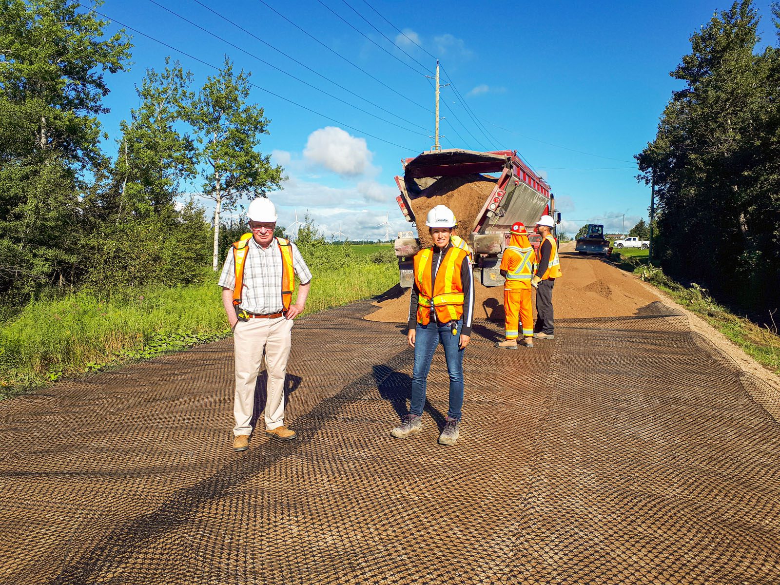 Workers on roadway with dumptruck spreading gravel